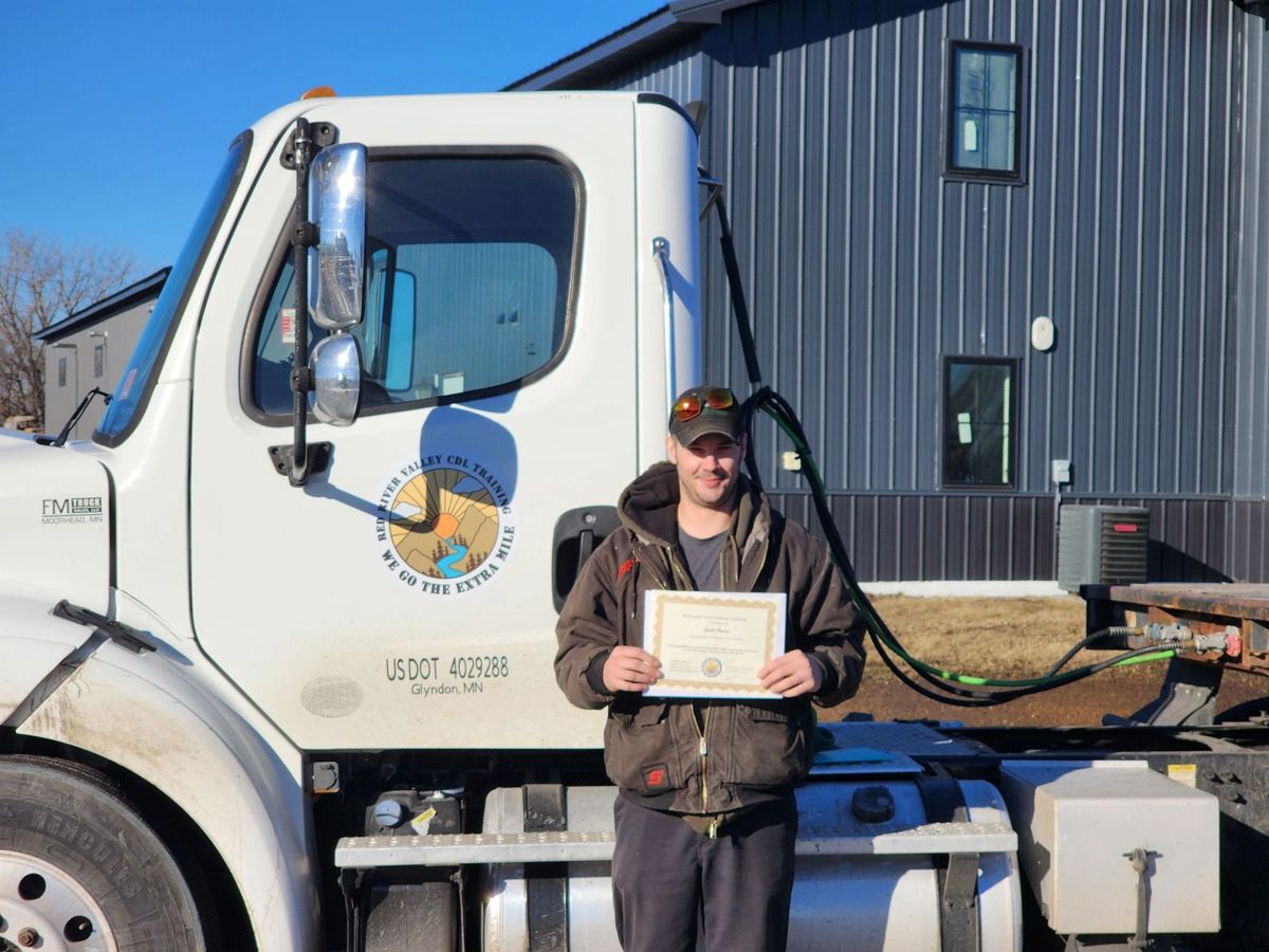 A Red River Valley CDL graduate holding his certificate in front of the training truck